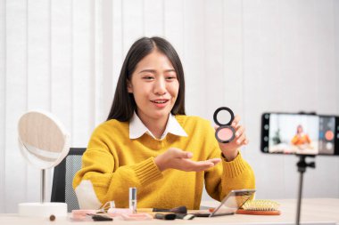 Güzel Asyalı kadın blogcu video kaydını kullanarak canlı yayın yapıyor ve evdeki kozmetikler için makyaj yapıyor..