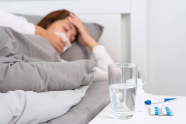 Yatakta yatan, baş ağrısı, ateş ve grip geçiren kadının masasına bir bardak su ve hap..