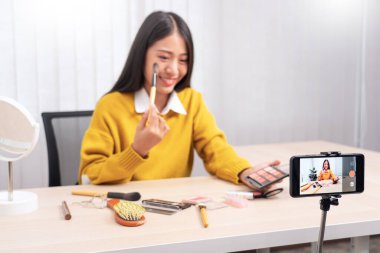 Güzel Asyalı kadın blogcu video kaydını kullanarak canlı yayın yapıyor ve evdeki kozmetikler için makyaj yapıyor..