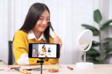Güzel Asyalı kadın blogcu video kaydını kullanarak canlı yayın yapıyor ve evdeki kozmetikler için makyaj yapıyor..