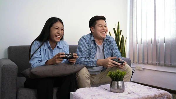Excited funny young couple playing video games holding game controller sitting on sofa having fun with new technology console online at home at night.