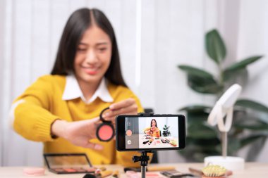 Güzel Asyalı kadın blogcu video kaydını kullanarak canlı yayın yapıyor ve evdeki kozmetikler için makyaj yapıyor..