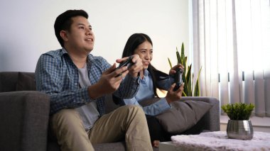 Heyecanlı genç çift video oyunları oynuyorlar. Oyun kontrolörleri kanepeye oturup geceleri evlerinde yeni teknoloji konsollarıyla eğleniyorlar..
