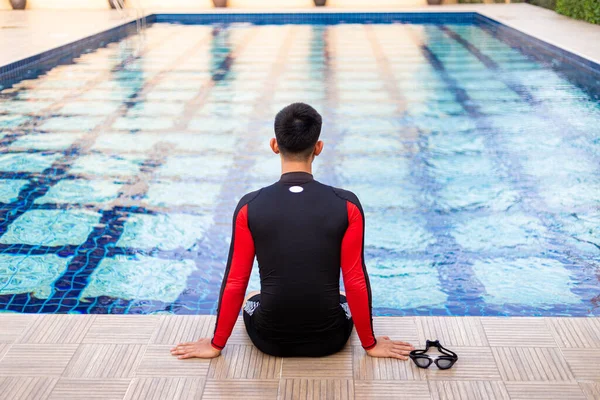 Sports and recreation concept a well-built boy sitting on the border of a blue-sky swimming pool enjoying the sunlight and lively weather.