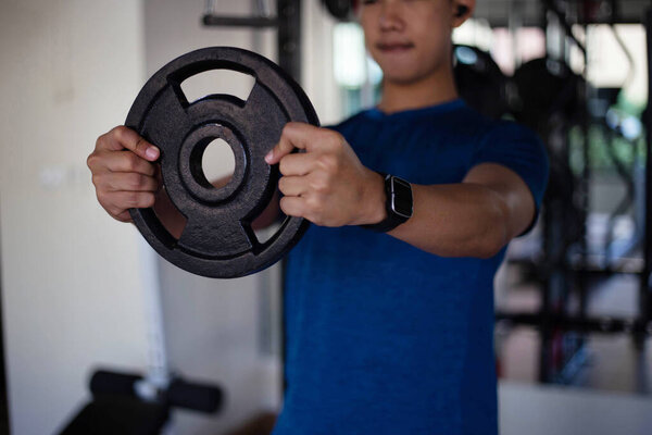 Training gym concept a muscled male teenager using both hands holding a heavy iron wheel.