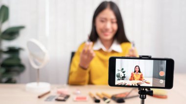 Güzel Asyalı kadın blogcu video kaydını kullanarak canlı yayın yapıyor ve evdeki kozmetikler için makyaj yapıyor..