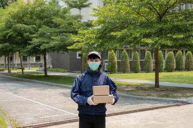 Paket teslimatı konsepti. Genç gönderici iki kutu paket kaldırıyor ve bu iki paketi atmak için dar bir caddenin ortasında duruyor..