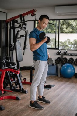 Spor salonu konsepti. Genç bir yetişkin, kaslı güçlü kolunu kullanarak spor salonunda bir dambılı yukarı bir aşağı kaldırıyor..