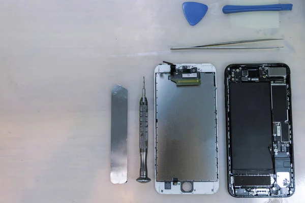 Phone repair concept the components of the smartphone separated into parts nearby the stainless tools including tweezers, an iron bar, and a tiny screwdriver.