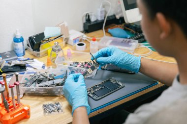 Telefon tamir konsepti. Elektronik kısmı seçen bir tamirci. Masadaki aletlerle cep telefonuyla monte etmek için..