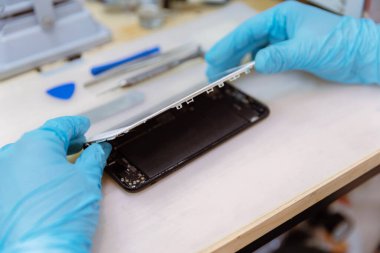 Telefon tamir konsepti, ahşap masadaki aletlerle akıllı telefonun vücudundan çıkarılan kırık bir ekran..