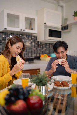 Mutlu Asyalı çift ev mutfağında sabah kahvaltısının tadını çıkarsın. Rahat bir hayat tarzı olan bir birliktelik sahnesi. Sağlıklı yemek mutluluğu.