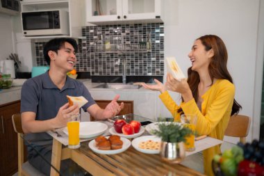 Neşeli Asyalı çift, parlak bir mutfak masasında nefis ev yapımı kahvaltının tadını çıkarıyor. Kahkahaları ve sıcak sohbetleri paylaşıyorlar. Huzurlu bir başlangıç.