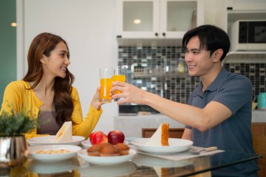 Mutlu Asyalı ortaklar, kahvaltıda aşklarını kutlayan taze meyve suyuyla kadeh kaldırır.