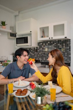 Yetişkin Asyalı kadın kahvaltı mutfağını paylaşıyor. Sağlıklı yiyecek taze meyve suyu parlak sabah ışığı mutlu ev hayatı sahnesi