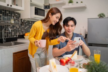Neşeli Asyalı ortaklar sağlıklı ev yemeği ev ortamında mobil iletişimi kurarlar.