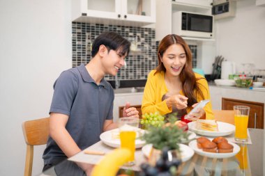 Neşeli Asyalı çift kahvaltı saatinin tadını çıkarıyor ev görüşü telefon içeriği birlikte rahatlamış sabah yemeği deneyimi