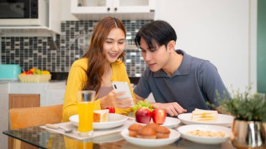 Yetişkin kadın rahat bir sabah yemeğinin tadını çıkarıyor. Mutfak masasında dijital içerikle ilgilenen mobil bir cihaz görüntüsünü paylaşıyorlar. Bağlantı anı.
