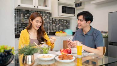Neşeli Asyalı yetişkinler parlak mutfakta sağlıklı bir yemek ve hamur işi paylaşırlar. Mutlu etkileşim samimi bir aile ortamı yaratır..