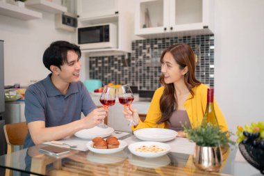 Mutlu bir Asyalı çift modern yemek masasında şarap kadehlerini kaldırıyor. Kahkahaları ve özel bir akşam yemeğini paylaşıyorlar.
