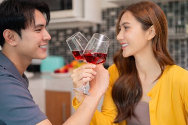 Genç Asyalı yetişkinler evde kırmızı şarapla neşeli bir tost paylaşırlar. Sevgi ve yakınlık gösteren özel bir olayı kutlayın.