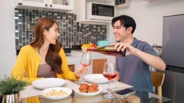 Genç Asyalı çift romantik bir akşam yemeğinden hoşlanıyor. Adam kadına kırmızı şarap koyuyor. Gülüşmeler modern samimi yaşam tarzını dolduruyor.
