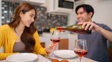 Mutlu Asyalı yetişkinler evde keyifli bir akşam geçirirler. Adam partneri için kırmızı şarap koyuyor. Birlikte rahatlatıcı bir akşam yemeğinin tadını çıkarıyoruz..
