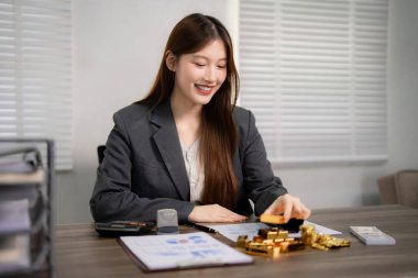 Profesyonel Asyalı kadın, altın külçeleri yatırım masasını yönetirken gülümsüyor. Finansal strateji uzmanı değerli metalleri idare ediyor..