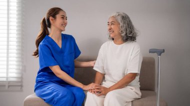 Genç Asyalı hemşire yaşlı hasta profesyonel bakıcıya hassas bakım sunuyor. Empati ve refakatçilik gösteriyor. Huzur ve huzur sağlamak için yaşlı sağlık hizmetlerini destekliyor.