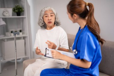 Yaşlı Asyalı kadın, genç hemşirelerden tavsiye ister. Profesyonel bakıcı sağlık değerlendirmesi sunar ve sağlık çözümleri sunar. Yaşlılara adanmış destek.