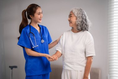 Genç Asyalı tıp uzmanı, huzur evindeki yaşlı bayana yardım ediyor. Şefkatli bakım ve destek sağlıyor..