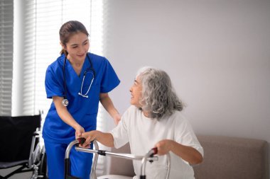 Bakımlı Asyalı hemşire yaşlı kadın hastaya nazikçe yardımcı olur. Walker bağımsız hareket kabiliyetini ve evde olmayı teşvik eder.