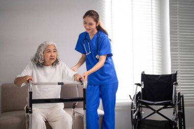 Bakıcı hemşire, yaşlı bir hastaya, bağımsızlık ve iyileşmeyi destekleyen parlak bir odada yürüteç kullanarak nazikçe yardım eder.