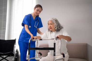 Yaşlı kadının ayakta durmasına Asyalı hemşire yardım ediyor. Kendini adamış bakım güvenli bir ortamda hareket özgürlüğünü geri kazanmayı teşvik eder