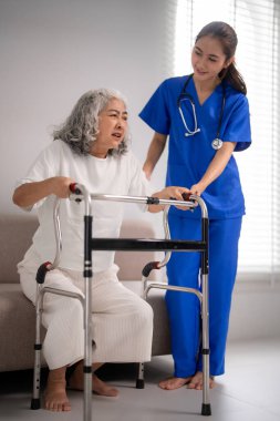 Merhametli Asyalı hemşire, yaşlı kadına tıbbi yürüteç kullanmasında yardımcı olur. Hasta hareketliliğinin iyileştirilmesi için gerekli desteği sağlar.