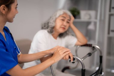 Genç Asyalı hemşire, Walker empatisi ve ev sağlığı hizmetlerinde desteği olan düşünceli yaşlı kadına şefkatli bir el konforu sunuyor.