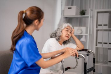 Genç Asyalı hemşire, Walker 'ın yaşlı hastalarına teselli sunuyor. Şefkatli sağlık uzmanı ev ziyareti sırasında destek sağlıyor. Geriatrik bakım yardımı.