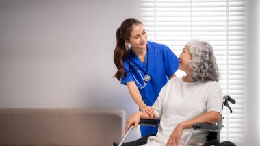 Asyalı hemşire, tekerlekli sandalyedeki yaşlı kadına şefkatli destek veriyor. Profesyonel tıbbi yardım, evdeki hastanın refahını artırıyor.