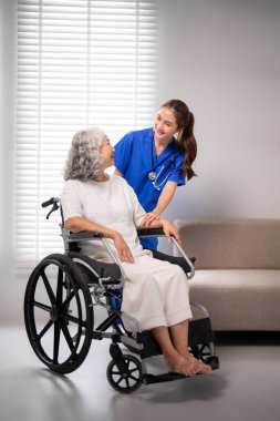 Genç Asyalı hemşire tekerlekli sandalyedeki yaşlı kadına yardım ediyor. Şefkat, sıcak bir gülümsemeyle sergilenir. Kıdemli sağlığı destekliyorum. Profesyonel tıbbi yardım sağlandı.
