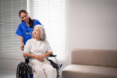 Merhametli yetişkin hemşire yaşlı Asyalı kadın hasta tekerlekli sandalyesine yardım ediyor. Hem mutlu, hem de kaliteli tıbbi destek içerideki huzur ortamını yansıtıyor.