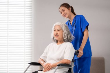 Genç Asyalı hemşire, tekerlekli sandalyedeki yaşlı kadına destek oluyor. Profesyonel sağlık hizmetleri, yaşlılara yardım, kıdemli sağlık hizmetleri.