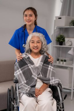 Asyalı hemşire yaşlı kadına şefkat gösteriyor. Yaşlı hasta tekerlekli sandalyede oturuyor. Destekleyici sağlık uzmanı yaşlılara rahat hissettirir.