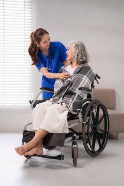 İlgilenen Asyalı hemşire içeride tekerlekli sandalyede oturan yaşlı bir hastaya yardım ediyor. Sağlık ve konfor sağlayan yaşlılara şefkat.
