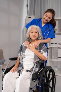 Kendini işine adamış Asyalı hemşire, tekerlekli sandalyede oturan yaşlı kadına, profesyonel ev sağlığı hizmetleri ve empatik hasta desteği sunuyor.