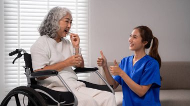 Profesyonel bakıcı, tekerlekli sandalyedeki yaşlı Asyalı kadına şefkat gösteriyor. Sağlık ve refah için günlük ilaçlar alıyor.