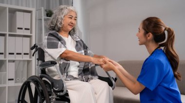 Kendini işine adamış genç Asyalı hemşire, tekerlekli sandalyedeki yaşlı kadına nazik ve empatik bir destek sağlıyor. Profesyonel bakım..