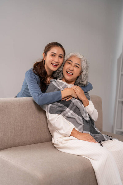 Азиатская дочь и пожилая мать разделяют любящие объятия. Они демонстрируют счастье и крепкую семейную связь в комфортной домашней обстановке.