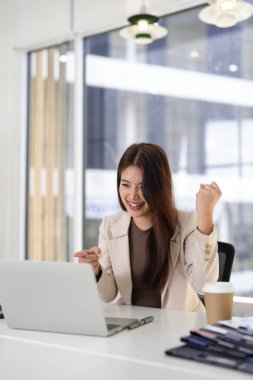 Mutlu Asyalı yetişkin kadın başarılı proje tamamlama modern ofis çalışma alanını başarıyla tamamladı. Profesyonel kadın işçi iş başarısı laptopunu kutluyor.