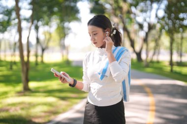 Asyalı kadın parkta yürümeyi seviyor kablosuz kulaklıklı müzik dinliyor fitness takibi için akıllı telefon tutuyor sağlıklı yaşam tarzını teşvik ediyor sağlıklı bir seçim.
