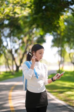 Genç Asyalı kadın dışarıda egzersiz yapmayı seviyor. Müzik ya da iletişim için kablosuz kulaklık ve akıllı telefon kullanıyor. Sağlıklı aktif yaşam biçimi.